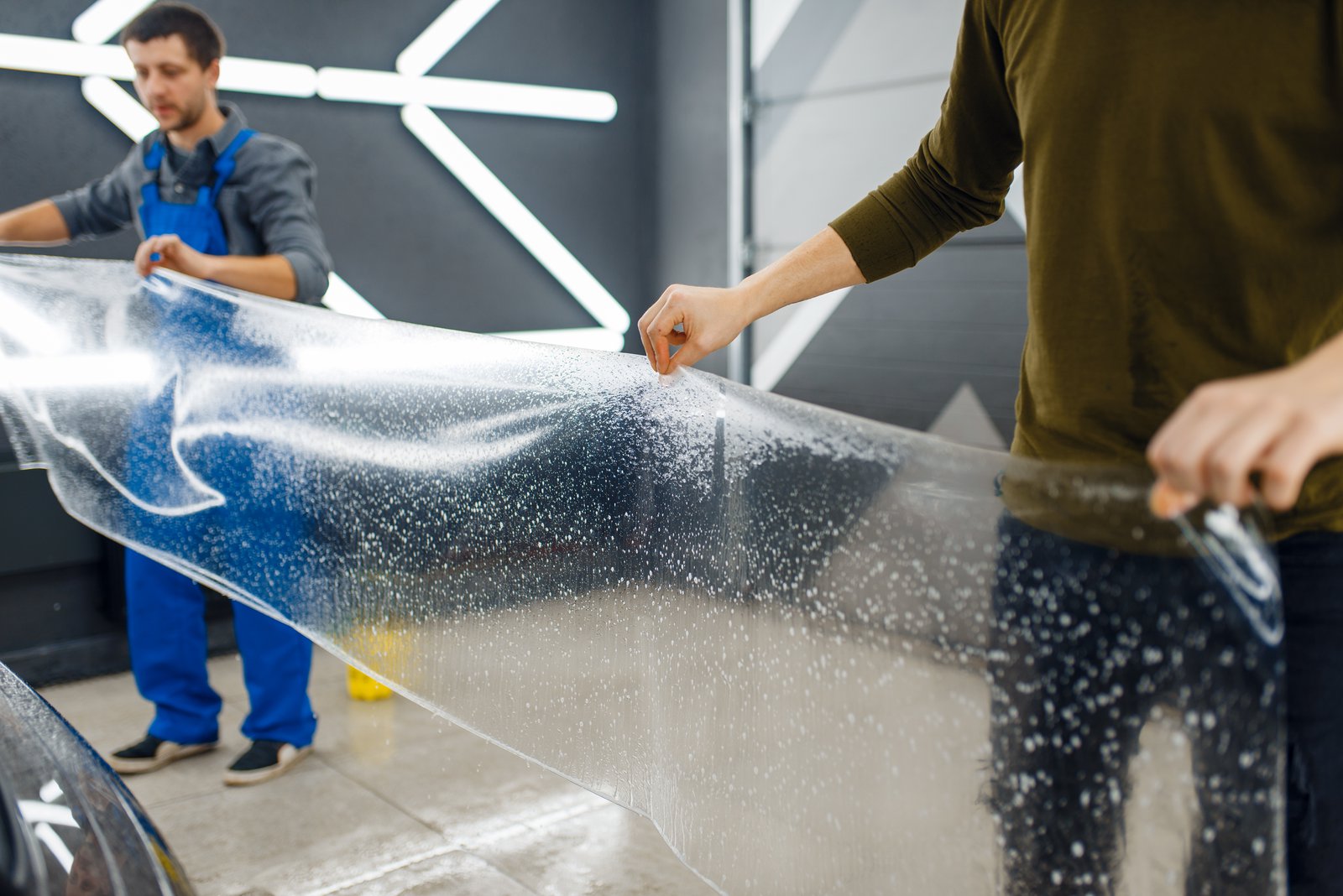 2 people installing clear PPF onto a car
